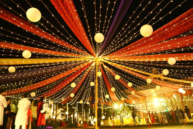 The venue canopy from below: orange, red and purple drapes radiating from a central point, threaded with fairy lights.